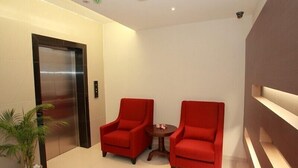 A modern lobby with two red armchairs, a small table, an elevator, and a potted plant. - Tai Ichi Hotel (Kuala Lumpur)