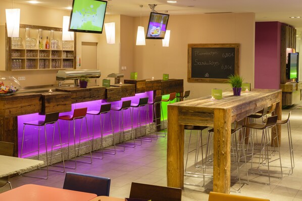 A bar area with a wooden counter, multiple bar stools, and a television screen. - Explorer Hotel Zillertal (Kaltenbach)