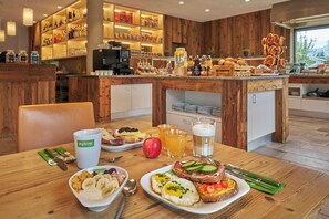A breakfast setting with a variety of food items, a coffee machine, and a bar area with bottles and snacks. - Explorer Hotel Zillertal (Kaltenbach)
