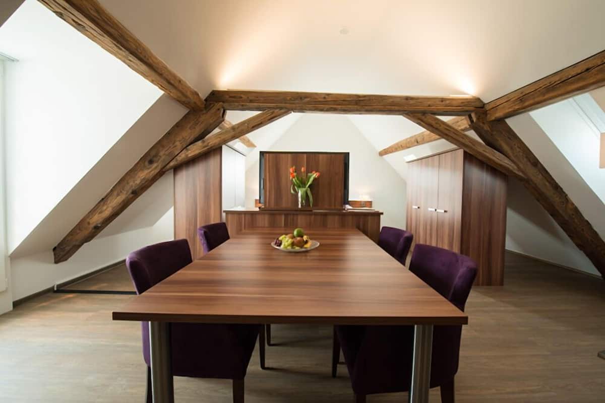 Uma sala de conferências com uma longa mesa de madeira, cadeiras roxas e uma fruteira como centro.