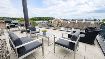 Une terrasse sur le toit, aménagée avec du mobilier d’extérieur, un barbecue et offrant une vue sur le paysage urbain.