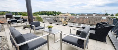 Een terras op het dak met buitenmeubilair, een barbecue en uitzicht op de stad.