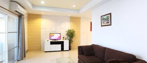 A modern living room with a brown sofa, a glass coffee table, and a flat-screen TV on a white cabinet.