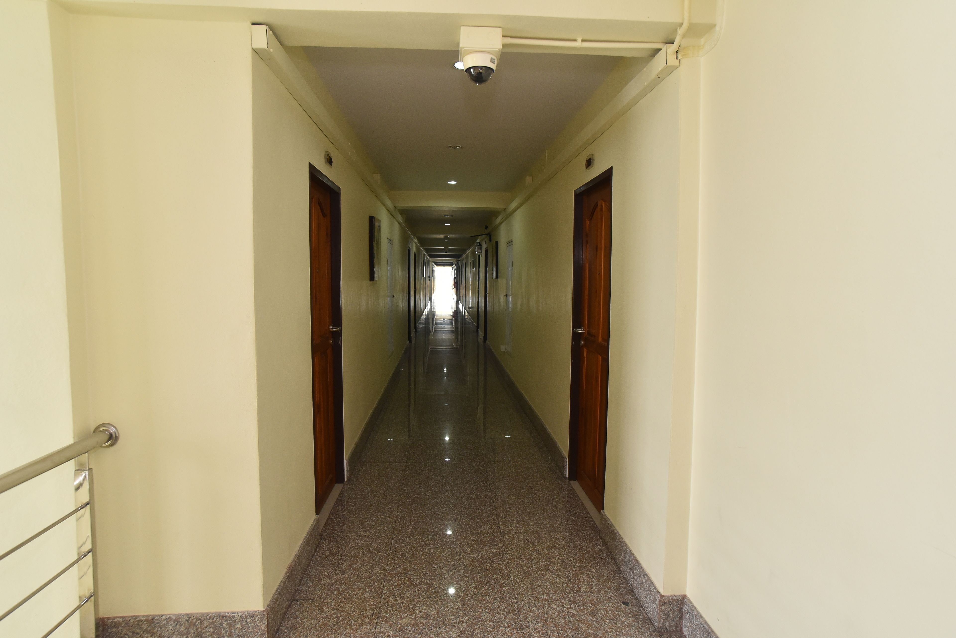 Um corredor comprido e estreito com soalho de pedra polida e portas de madeira de ambos os lados.