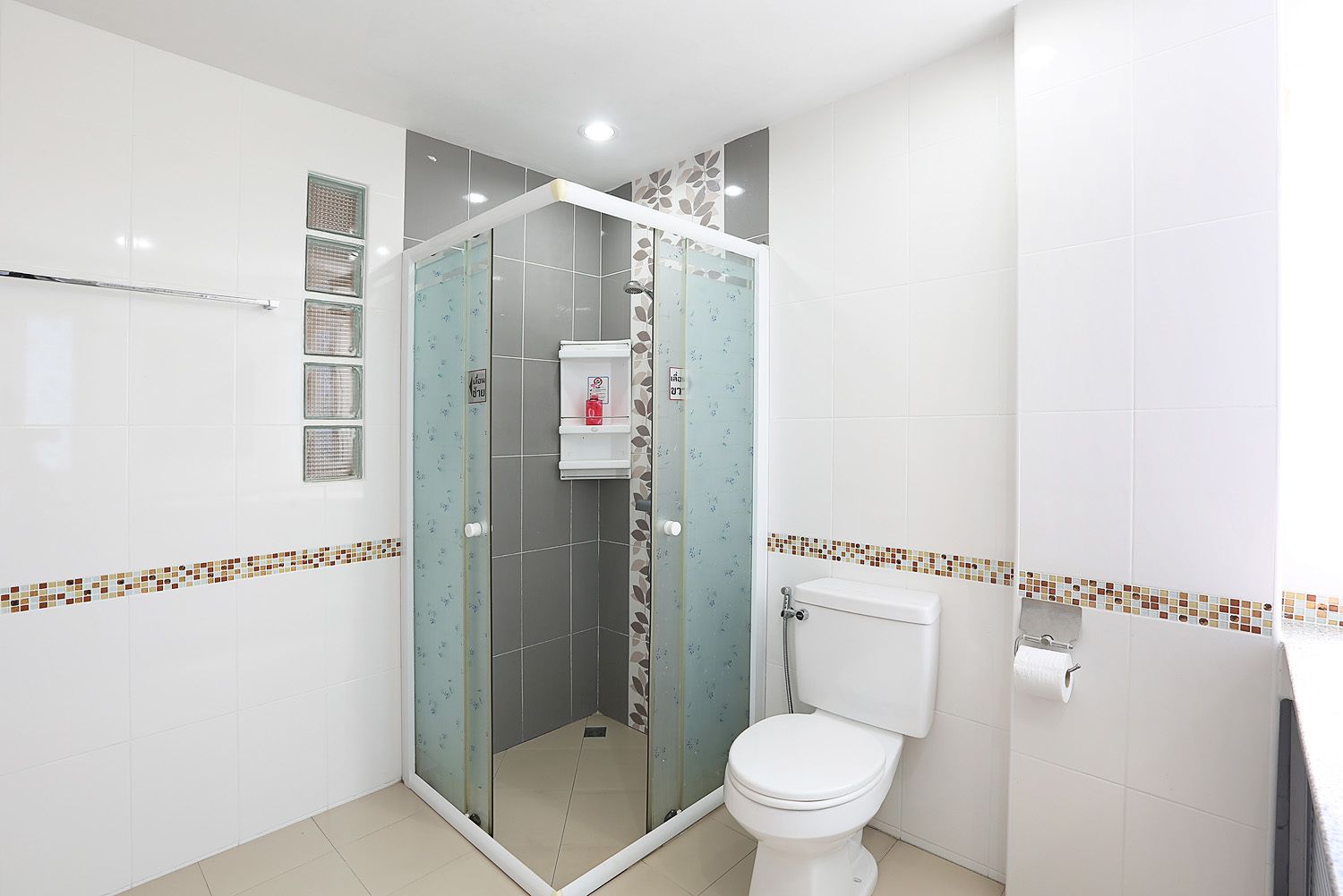 A bathroom with a glass-enclosed shower, a toilet, and a shelf with toiletries.