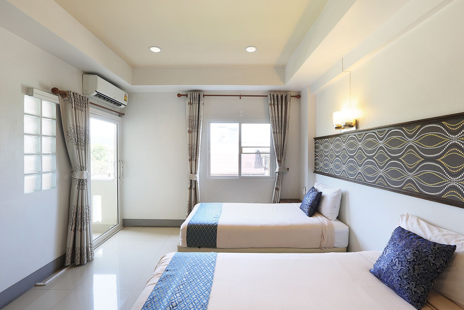 A hotel room with two beds, a large window, an air conditioning unit, and a patterned wall.