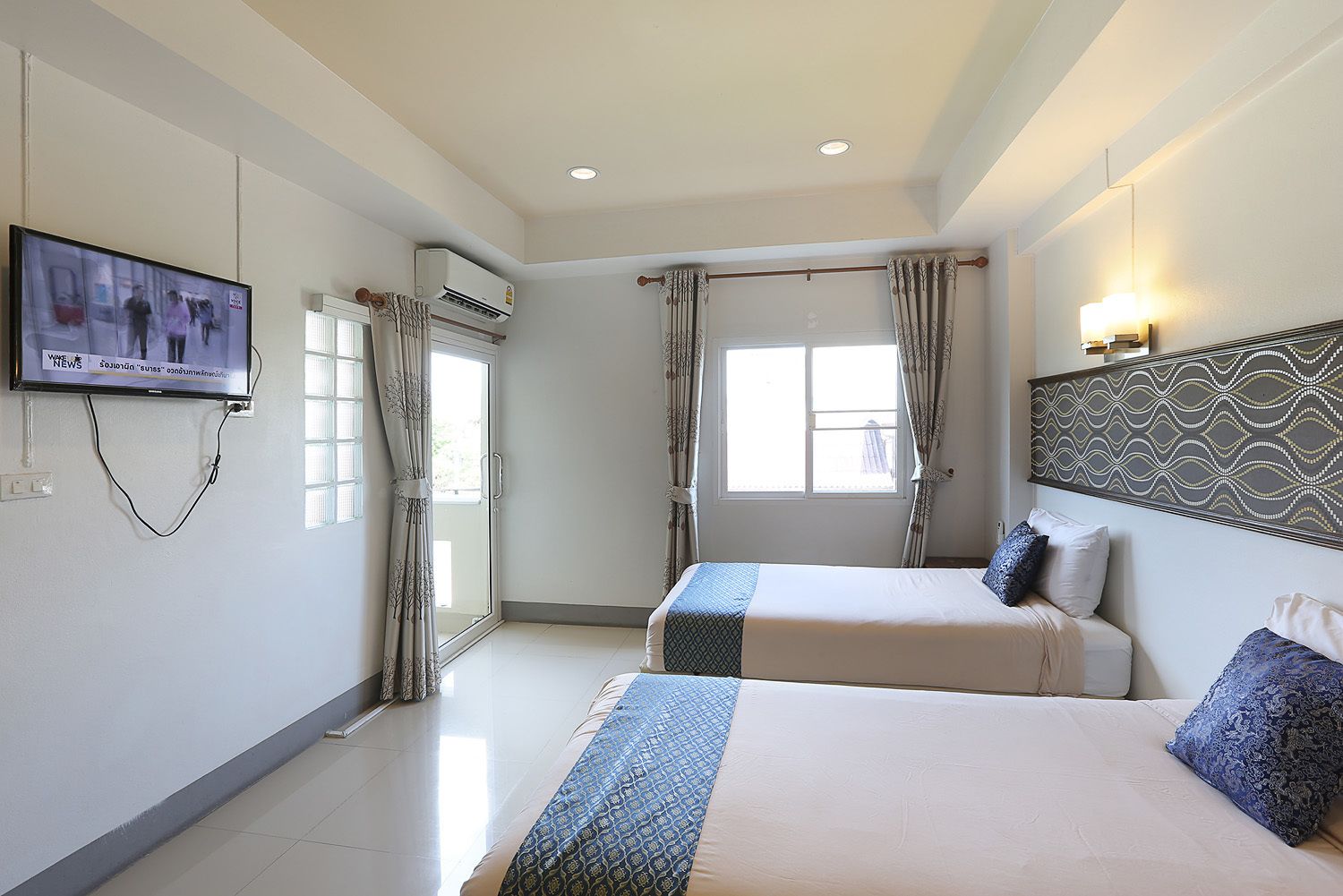 A hotel room with two beds, a TV mounted on the wall, and a window with curtains.