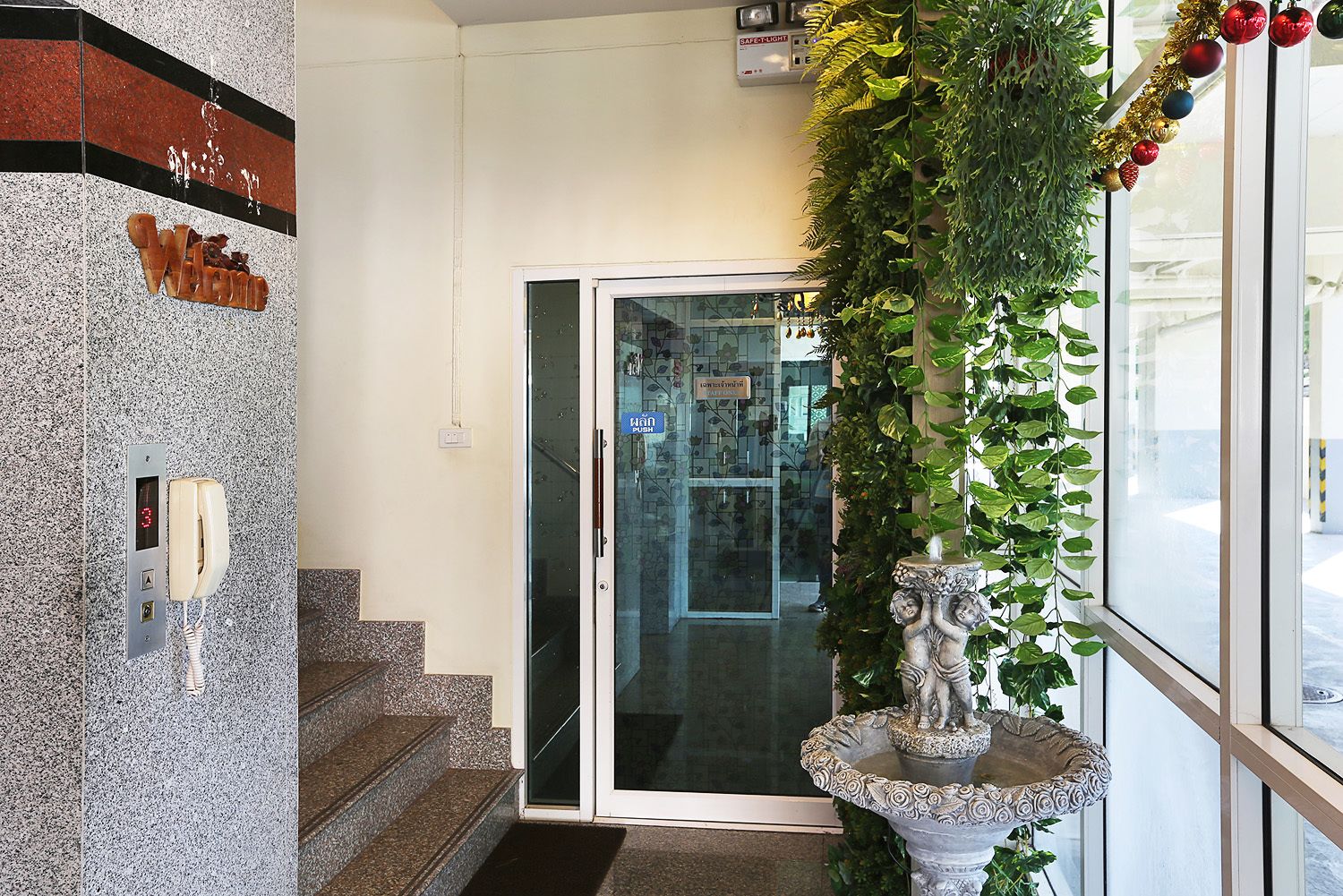 Entrada de un hotel con recepción, teléfono, escalera y una fuente decorativa.