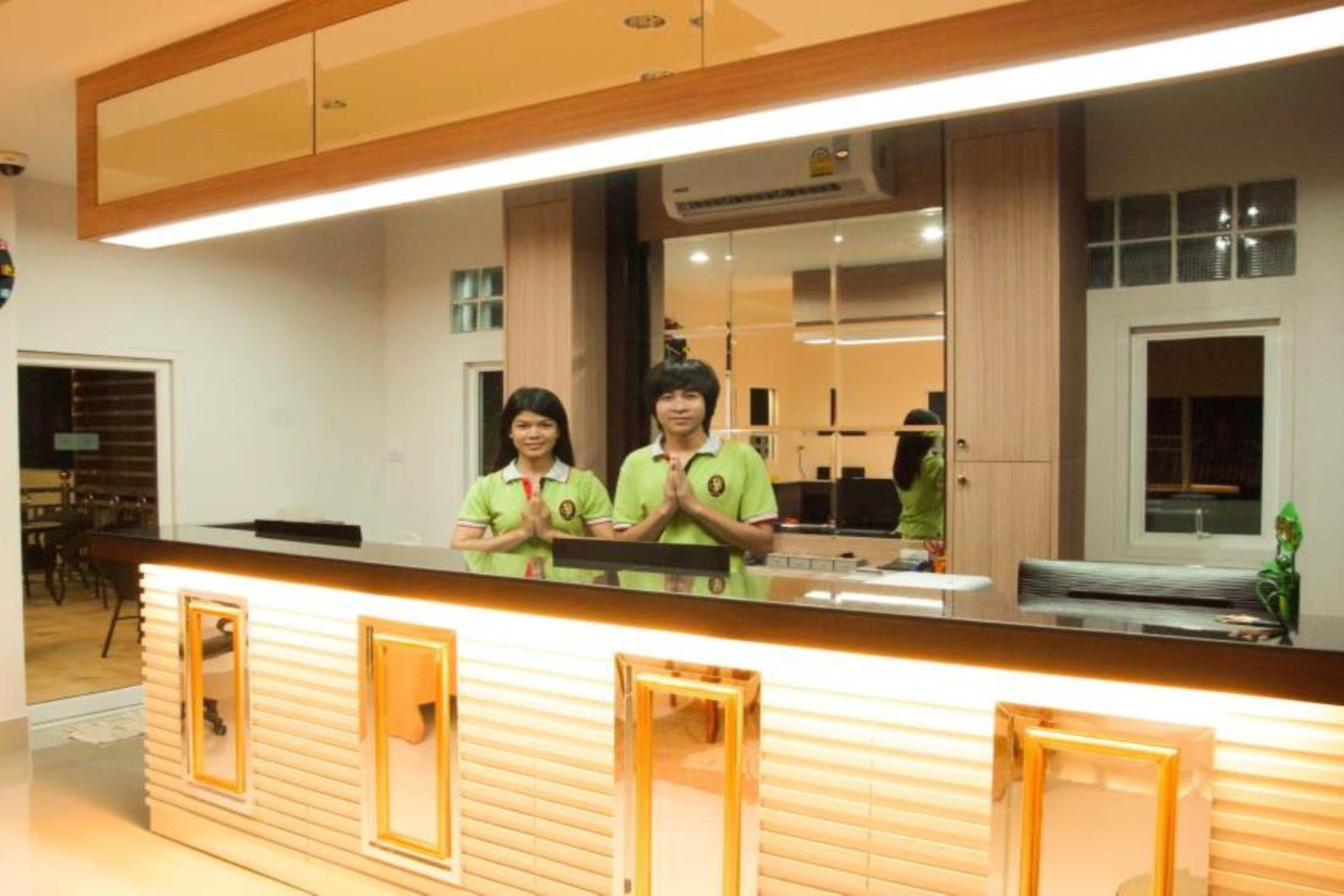 A reception desk with a wooden finish and glass panels, a large mirror above it, and a window to the right.