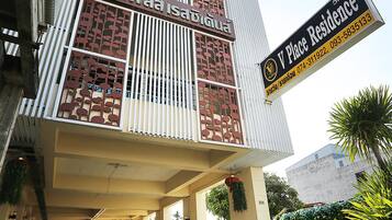 Um edifício com uma placa indicando 'V Place Residence' e uma galeria coberta com vasos de plantas.