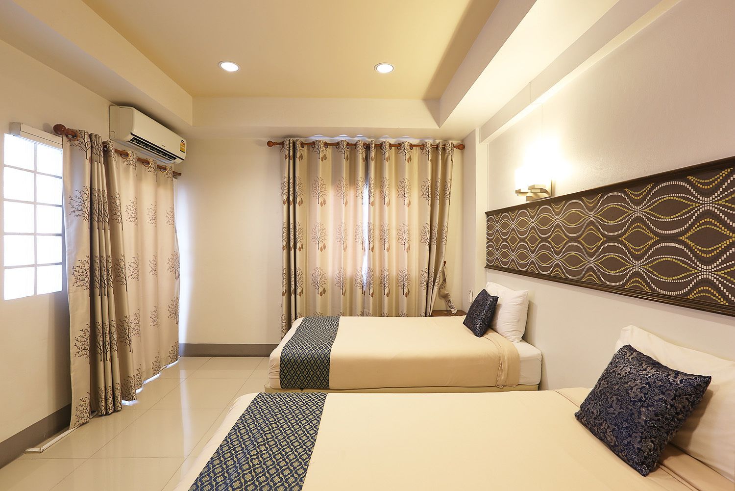 A hotel room with two beds, a patterned headboard, and an air conditioning unit.