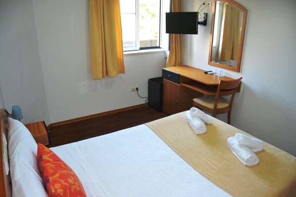 A hotel room with a bed, a desk, a chair, a TV, and a window with curtains.