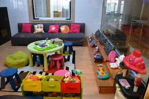 Uma sala de estar acolhedora, com um sofá, almofadas coloridas, uma mesa de centro e brinquedos infantis.