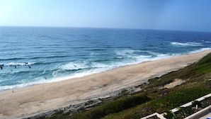 Une plage avec des vagues, une étendue de sable et quelques zones verdoyantes.