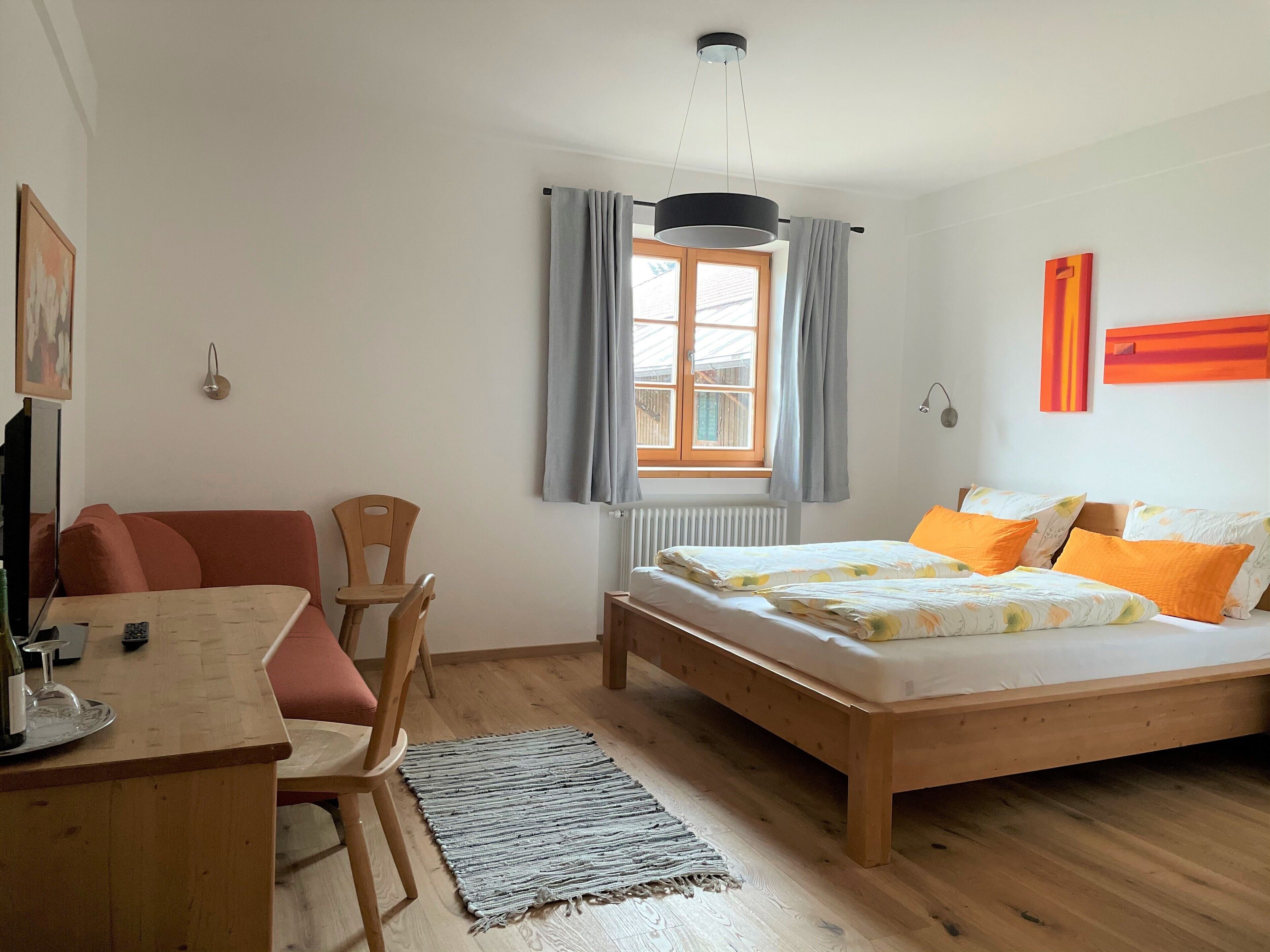 Ein Schlafzimmer mit einem Holzbett, einem Schreibtisch mit Stuhl, einem Fenster mit Vorhängen und einer Heizung.