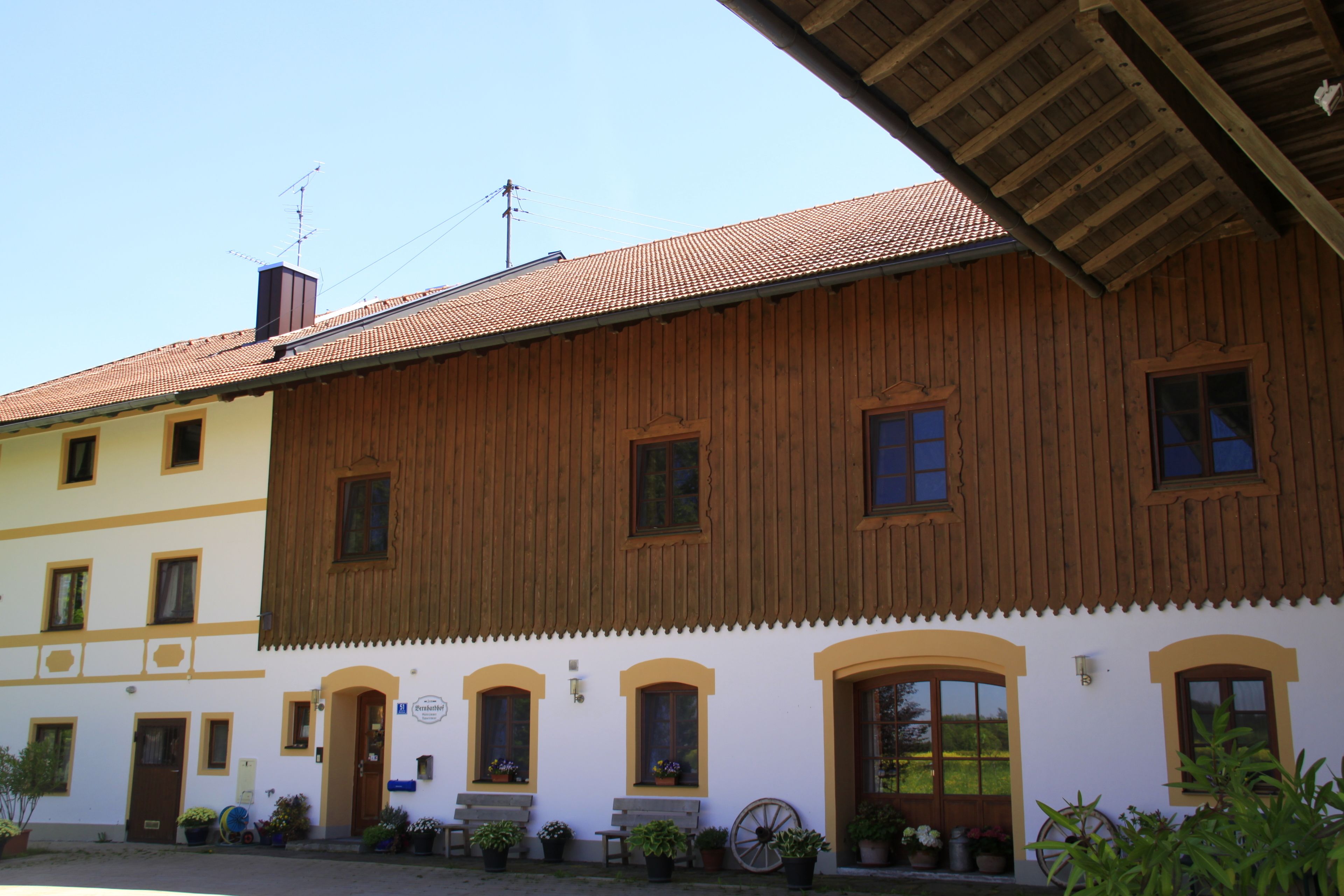 A traditional wooden building with multiple windows and doors, a tiled roof, and potted plants outside.