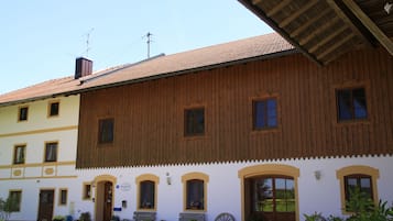 A traditional wooden building with multiple windows and doors, a tiled roof, and potted plants outside.