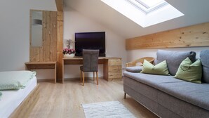 A bedroom with a skylight, a bed, a desk with a computer, a grey sofa, and a mirror. - Pension Bernhardhof (Otterfing)