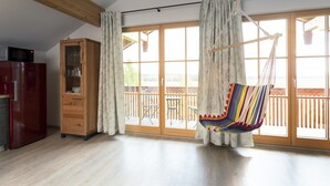 A spacious room with a wooden ceiling, a hanging chair, a wooden cabinet, and a sliding glass door leading to an outdoor deck. - Pension Bernhardhof (Otterfing)