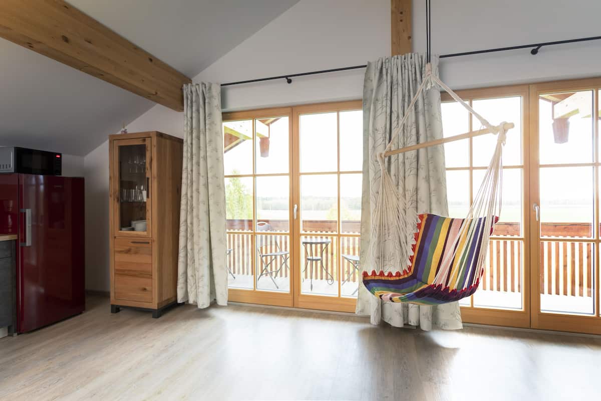Amplia habitación con techo de madera, una silla colgante, un mueble de madera y un ventanal corredero que da a una terraza exterior.