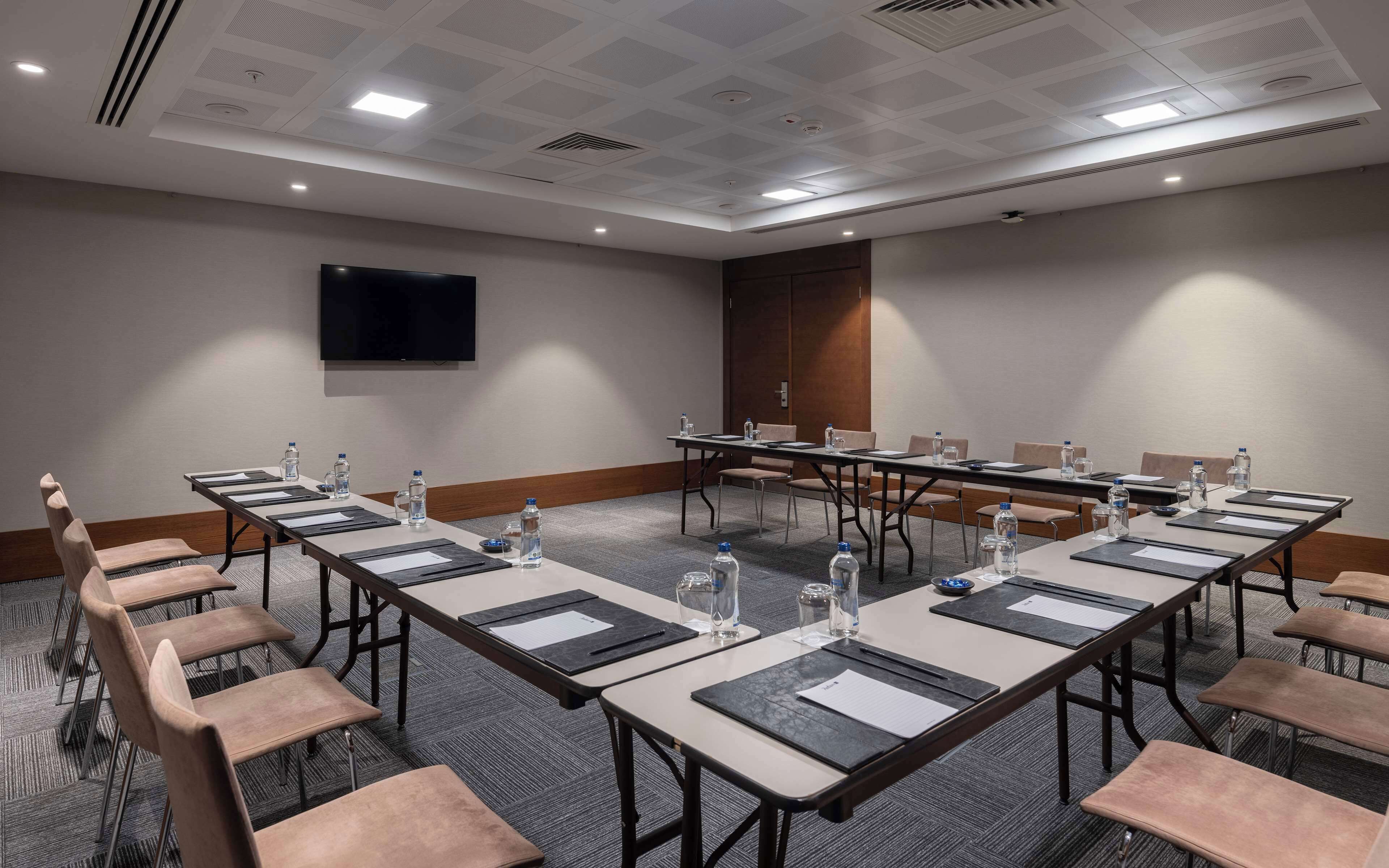 Un salón de conferencias con una larga mesa, sillas, botellas de agua y un televisor de pantalla plana en la pared.
