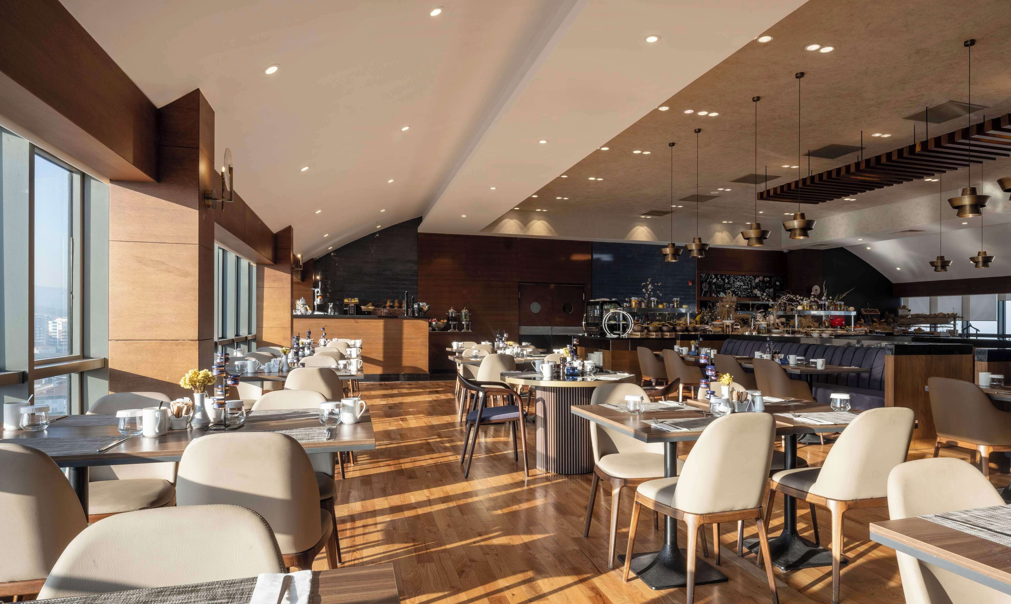 A modern restaurant with a high ceiling, wooden flooring, and a bar area.