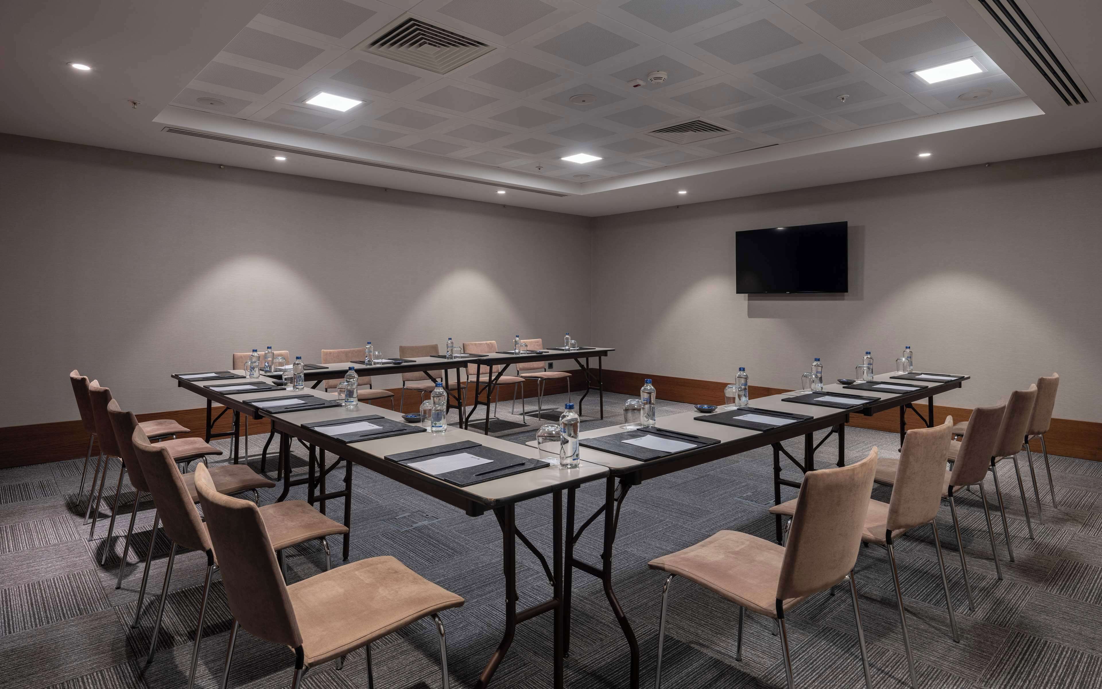 A conference room with a long table, chairs, water bottles, and a flat-screen TV on the wall.