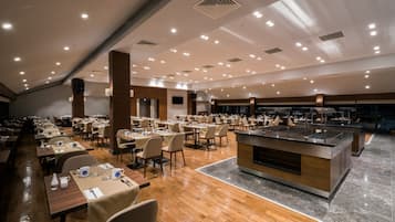 A spacious dining area with multiple tables and chairs, a central buffet station, and a high ceiling with recessed lighting.