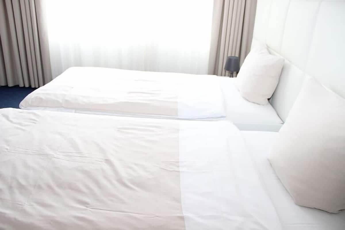 Quarto de hotel com duas camas, cabeceira e mesa de cabeceira.