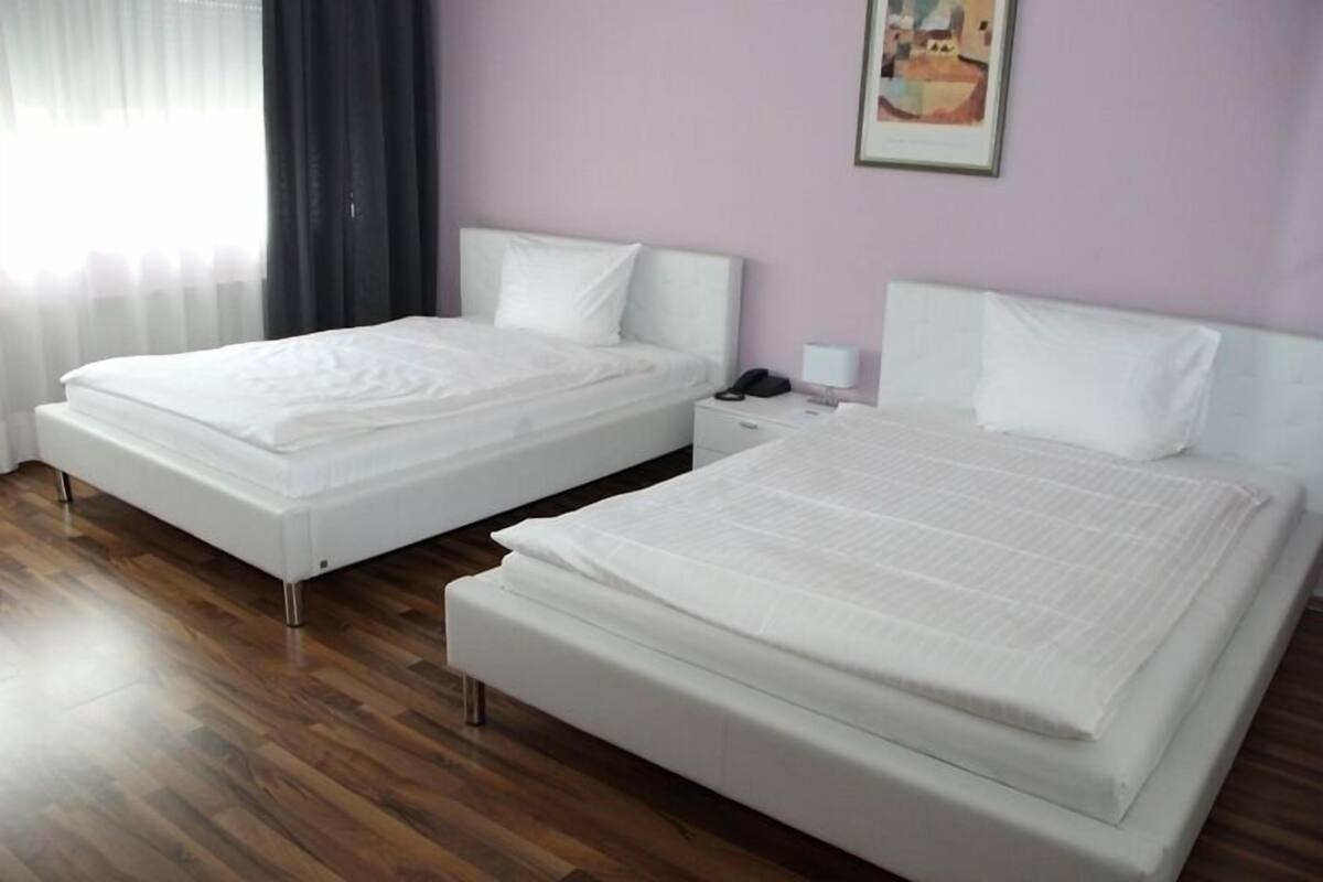 Quarto de hotel com duas camas de solteiro, uma mesa de cabeceira com abajur e um quadro na parede.