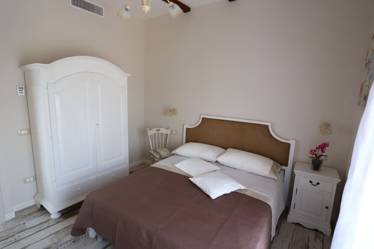 A bedroom with a bed, a wardrobe, a nightstand, and a wall-mounted light fixture.
