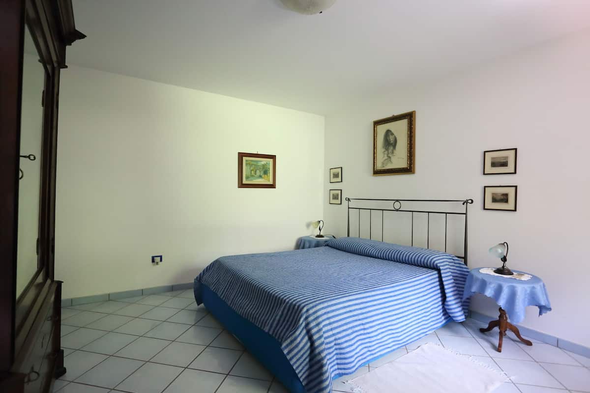 A bedroom with a bed, a small table with a lamp, and a few framed pictures on the wall.