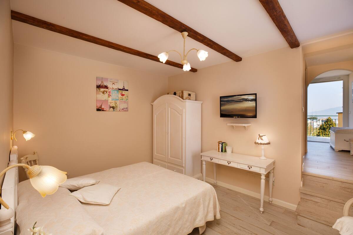 A bedroom with a bed, bedside table, TV, and a view of the outside.
