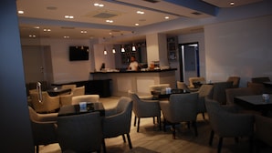 A modern restaurant with a bar area, seating arrangements, and a television mounted on the wall. - Hotel Mano (Sarandë)