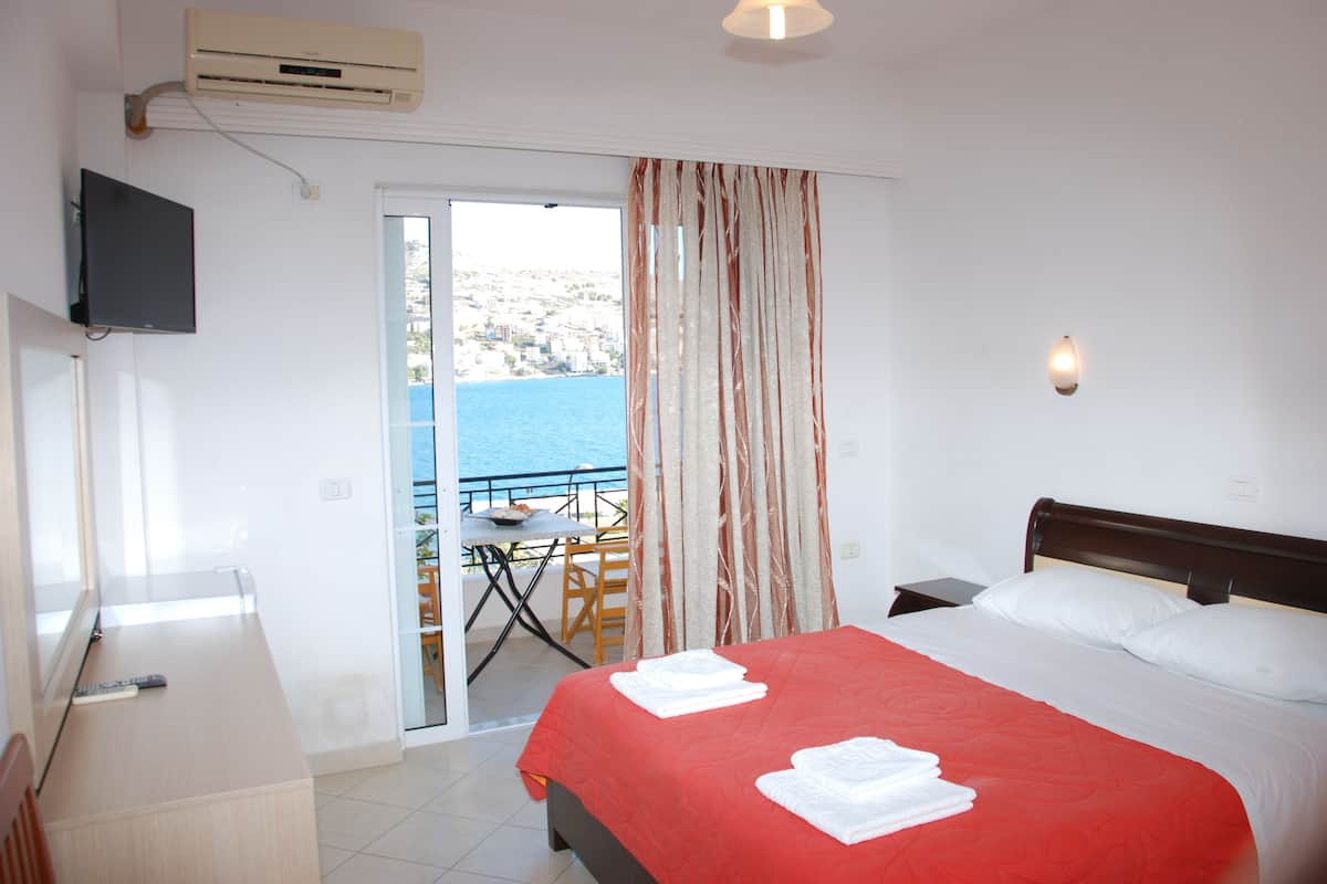 Une chambre d’hôtel avec un lit, une télévision, un balcon avec une table et des chaises, et une vue sur la mer.