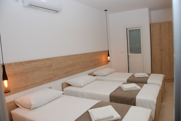 A hotel room with three single beds, each with a wooden headboard, white bedding, and a small table with a towel. - Hotel Mano (Sarandë)