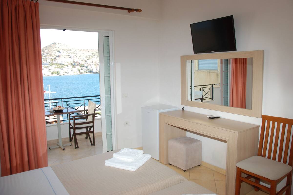 Une chambre avec un lit, un bureau, une chaise, une télévision et une vue sur la mer.