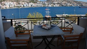 A balcony with a table and two chairs, overlooking a coastal cityscape with buildings and a ship. - Hotel Mano (Sarandë)