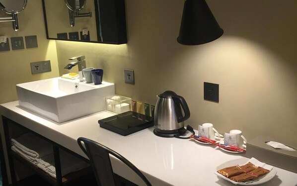 A hotel room with a white sink, a kettle, a tray, a cup, and a plate with snacks.