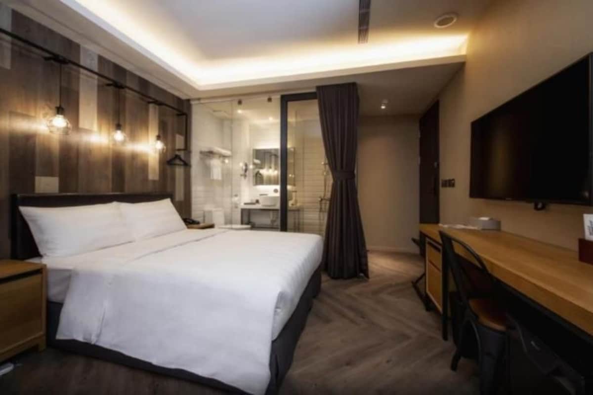 A modern hotel room with a large bed, a desk, and a TV.