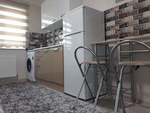 A compact kitchen with a washing machine, a refrigerator, and a metal bar stool. - Moonlight (Erzincan)