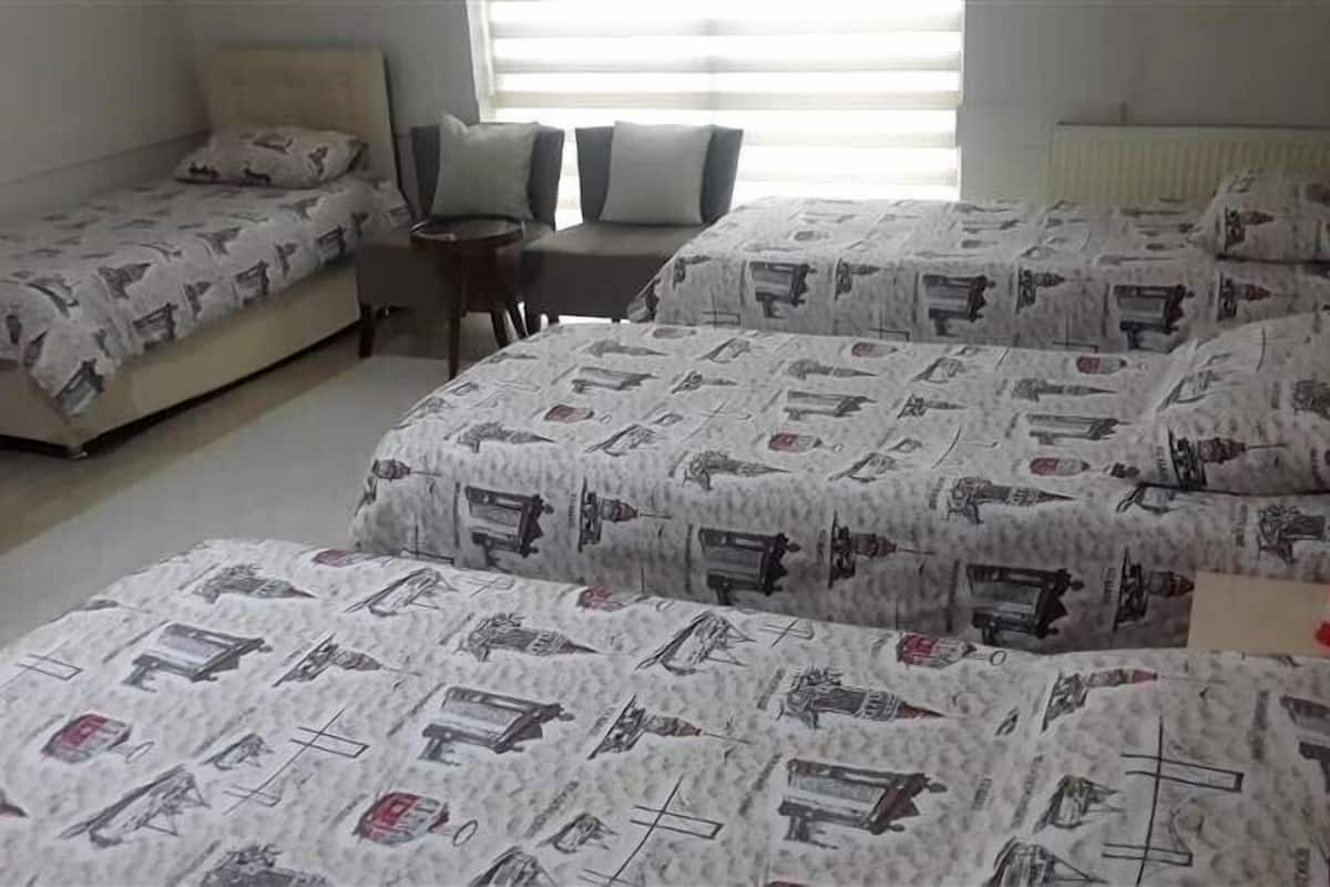 A room with three beds, each with patterned bedding, a small table, and a chair.