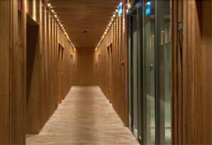 Un pasillo con paredes de madera y piso cubierto de alfombra, que conduce a una puerta de vidrio.