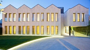 Un edificio moderno con fachada simétrica, ventanas amplias y zona de acceso pavimentada.