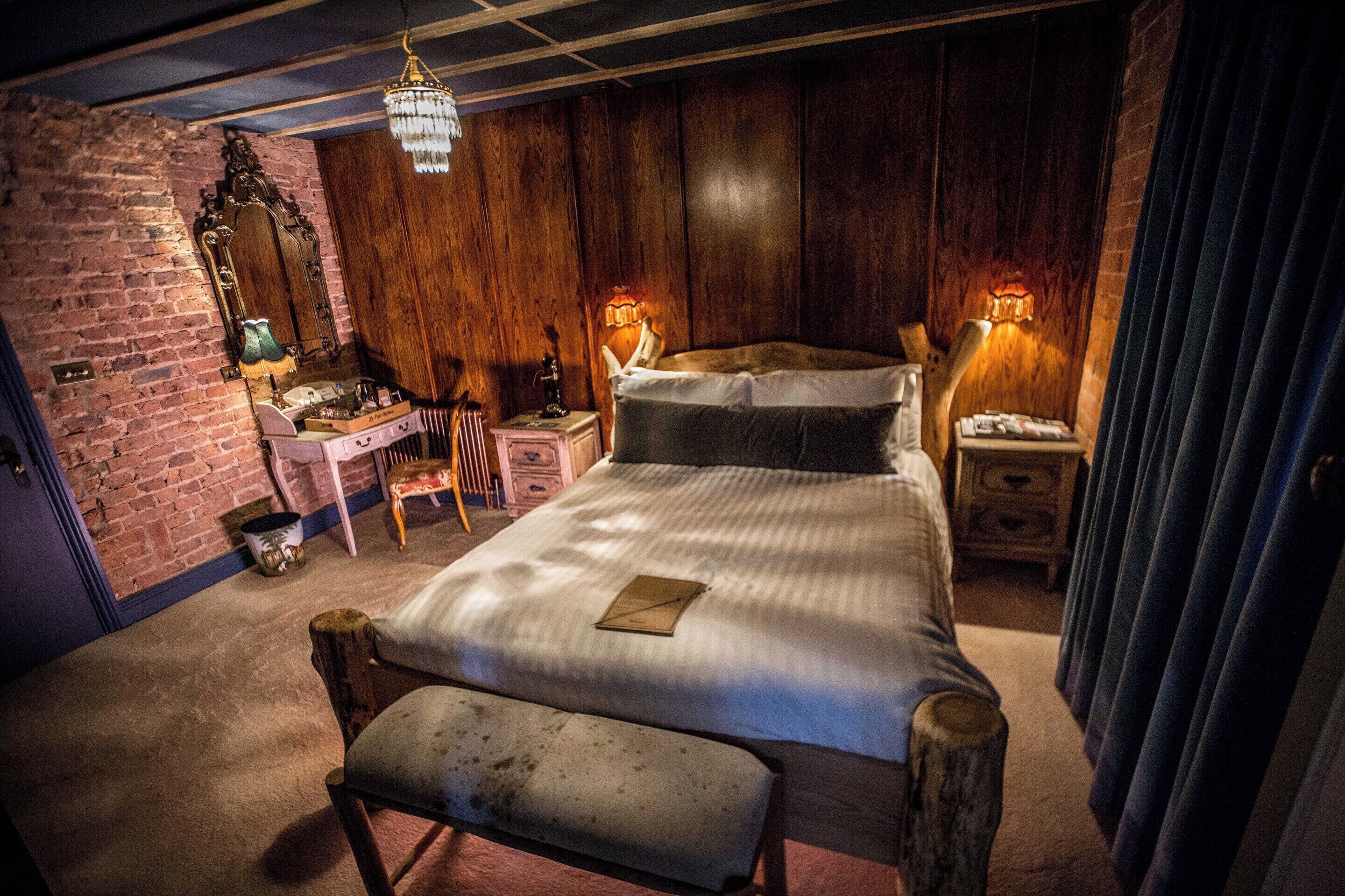 Een slaapkamer met een houten hoofdbord, een bankje, een bureau met spiegel en twee bedlampen.