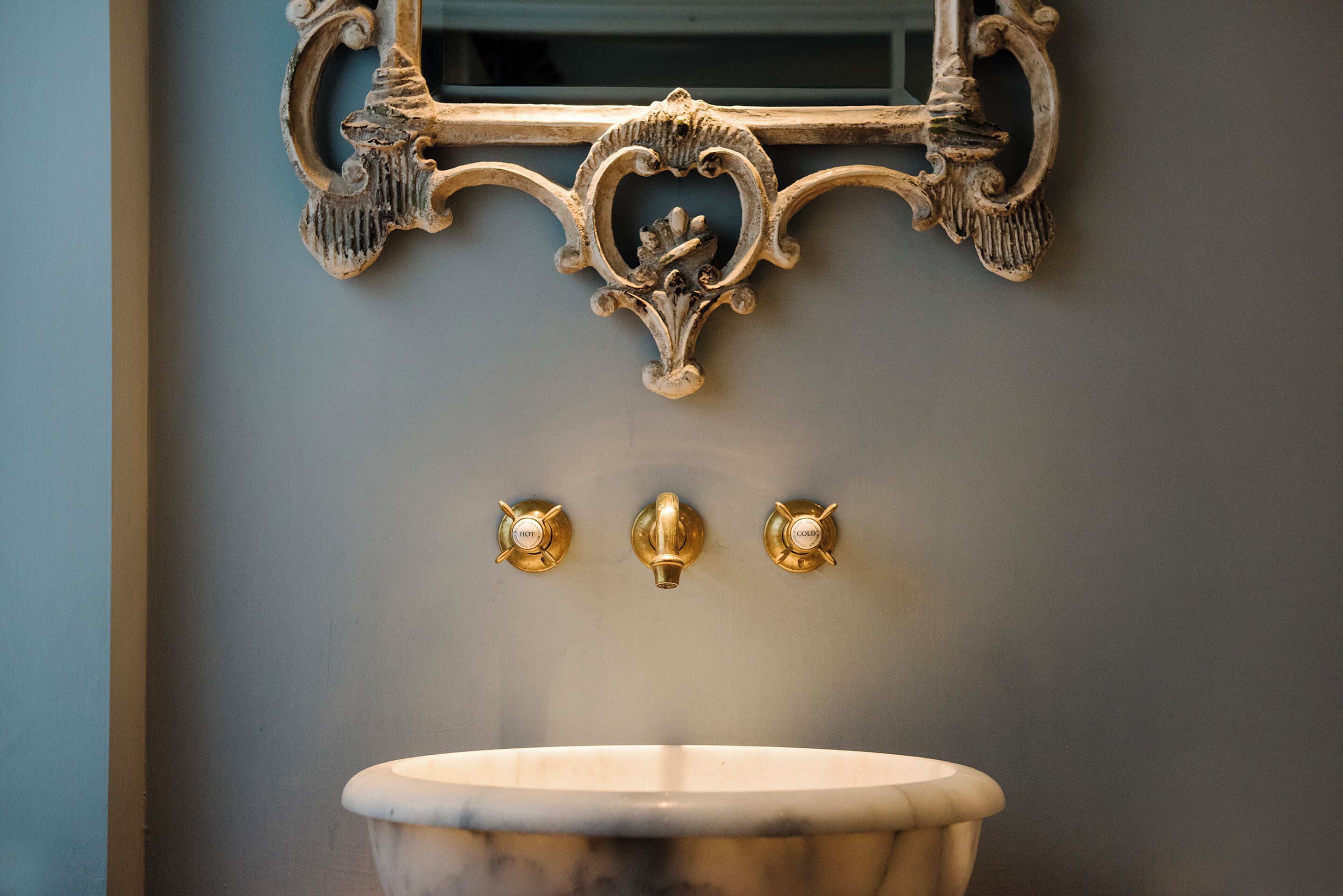 Un baño con lavamanos de mármol, grifos dorados y un espejo decorado.