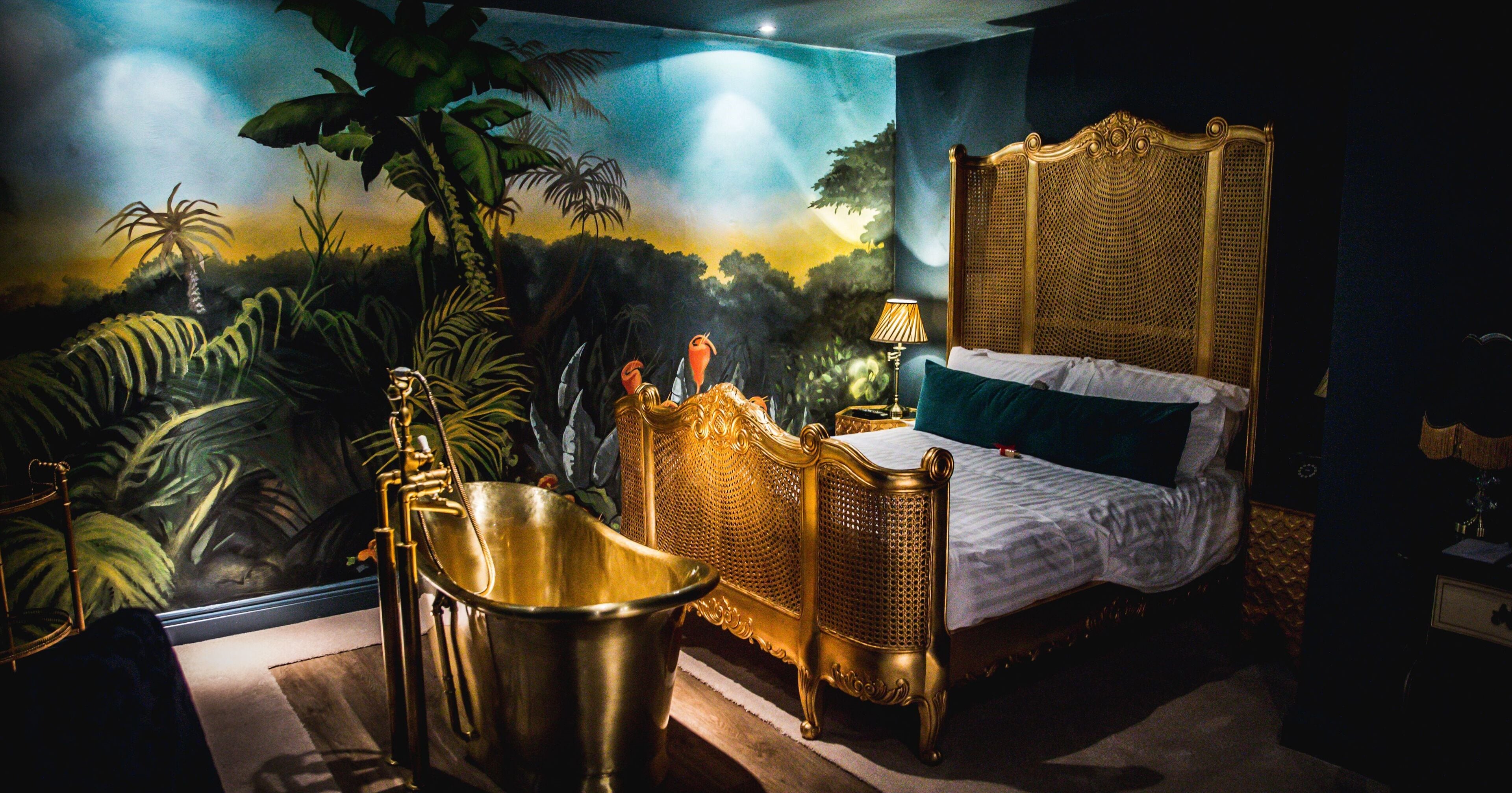 A luxurious bedroom with a large bed, a golden bathtub, and a mural of a jungle scene.