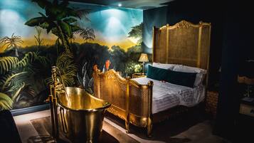 A luxurious bedroom with a large bed, a golden bathtub, and a mural of a jungle scene.
