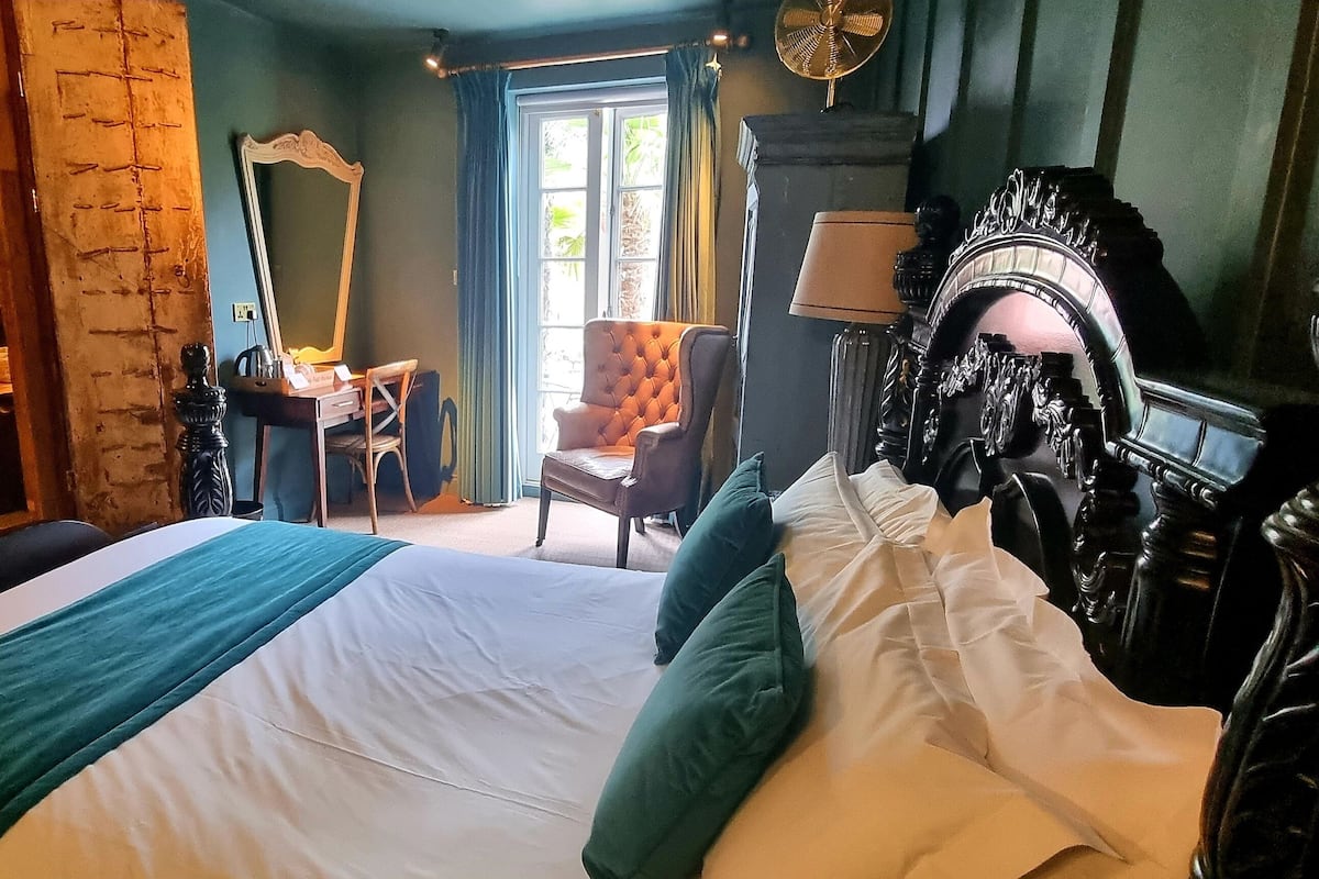 Une chambre à coucher avec un grand lit, une baignoire ancienne, une chaise, un miroir et une lampe.