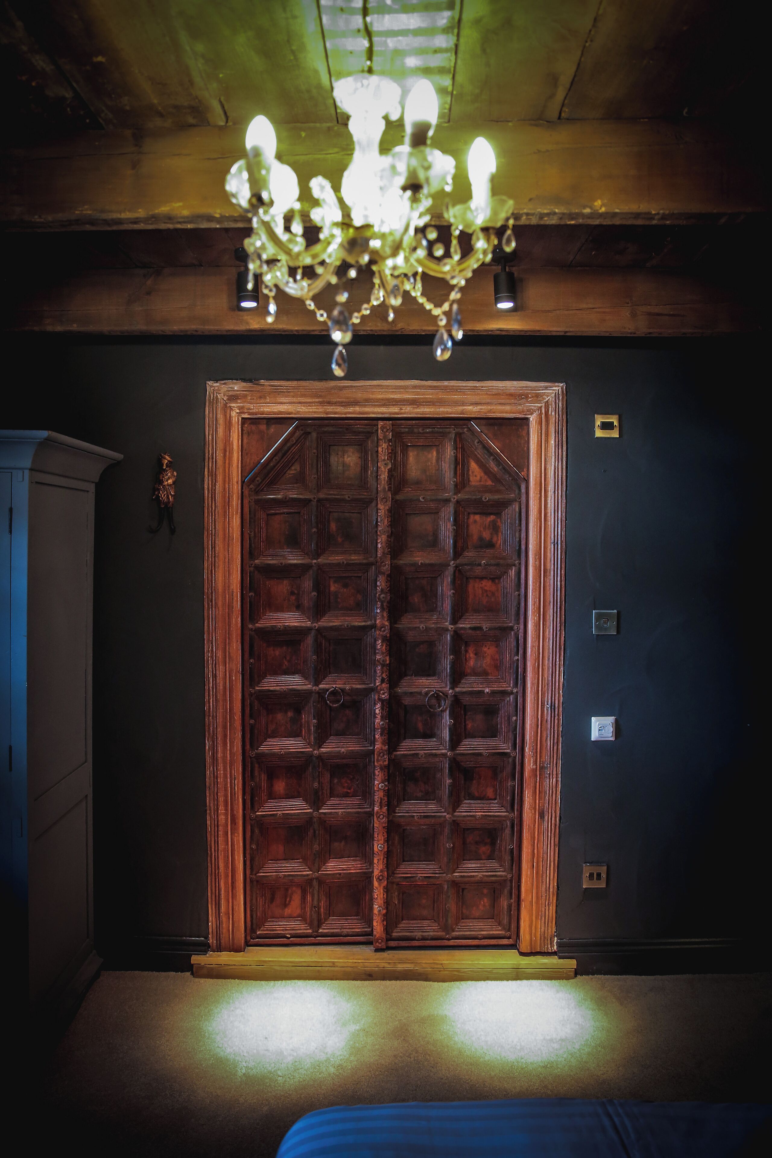 A room with a large wooden door, a chandelier, and a bed.